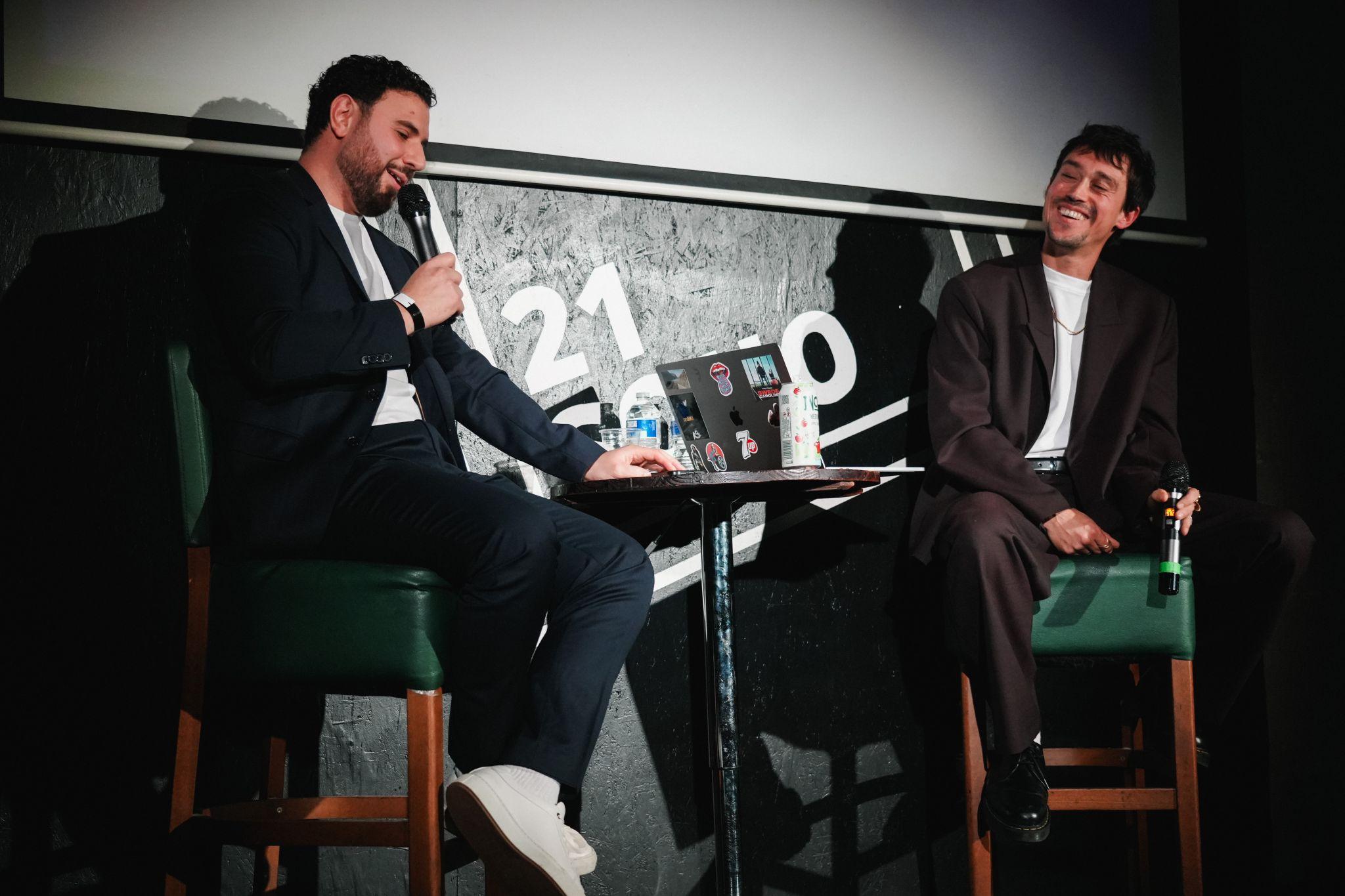 Two speakers in conversation on stools in front of the 21Soho mark at the DEADBEAT party