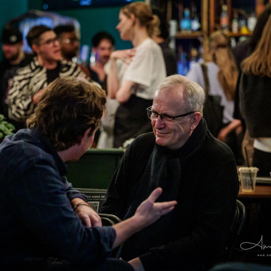 Two attendees in conversation between sessions at the FFWD conference, the bar behind them