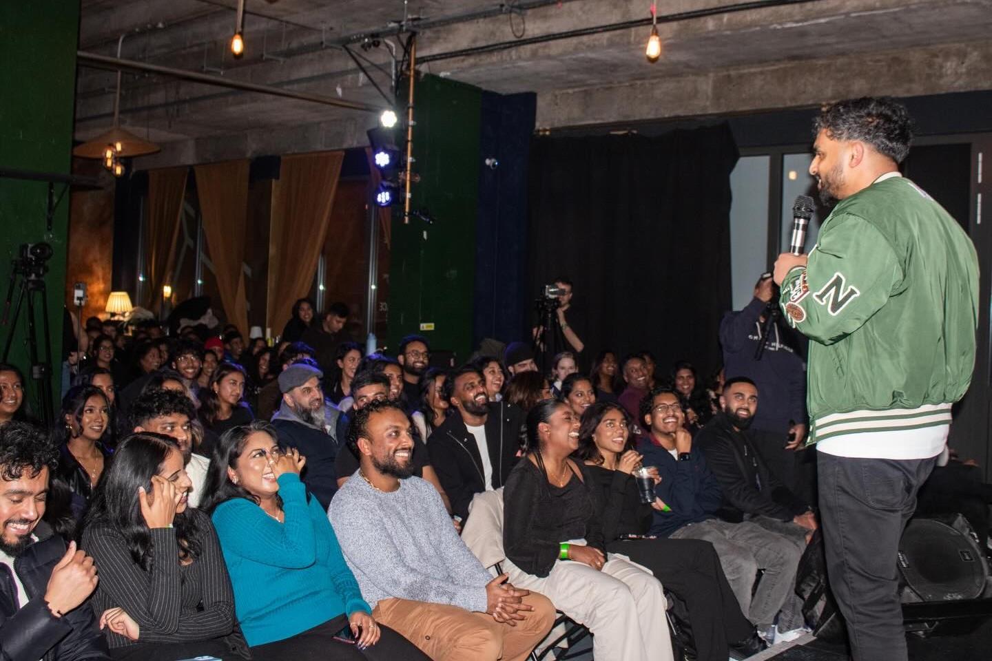 A comedian performing to a packed audience at a South Asian Comedy Night in the Main Room